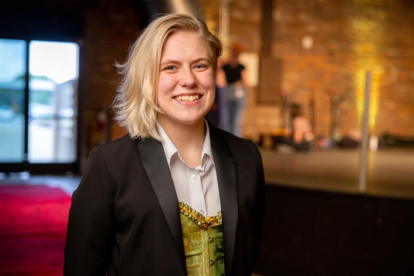 A young woman wearing a black blazer and a white and green top smiles